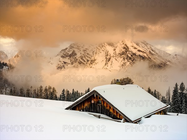 Snow-covered Priesbergalm in front of cloud-covered Watzmann