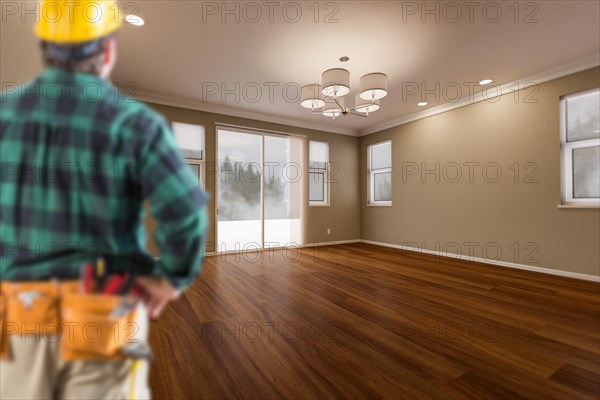 Contractor in hard hat and construction belt facing newly remodeled house room