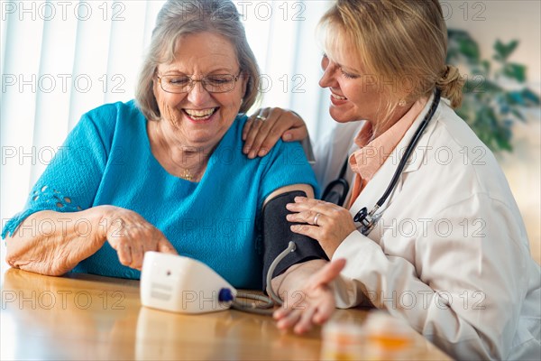 Senior adult woman learning from female doctor to use blood pressure machine