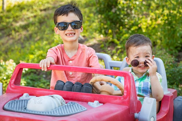 Young mixed-race chinese and caucasian brothers wearing sunglasses playing in toy car