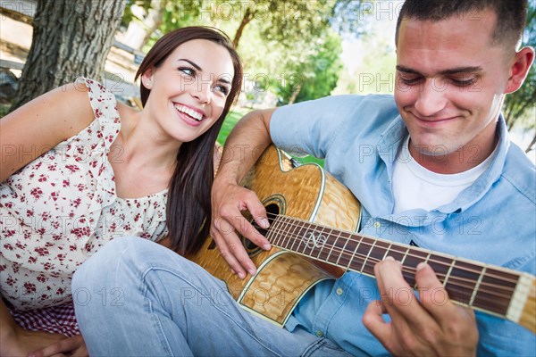 Young adult man playing guitar for his girlfriend in the park