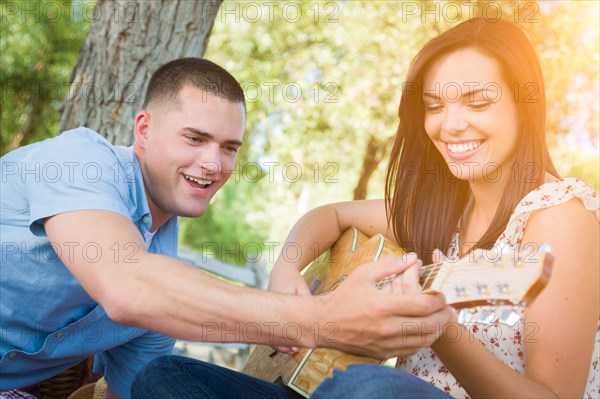 Handsome young man teaching mixed-race girl to play guitar at the park