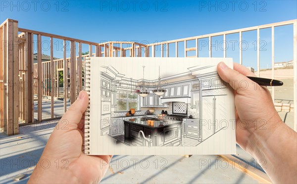 Male hands holding pen and pad of paper with custom kitchen illustration inside construction framing