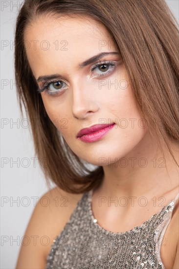 Portrait einer Huebschen jungen Frau mit langen Haaren und dezentem Make-Up vor weissem Hintergrund im Studio. Das glitzernde Shirt passt zum dezenten Make-Up. Der Blick richtet sich zur Kamera