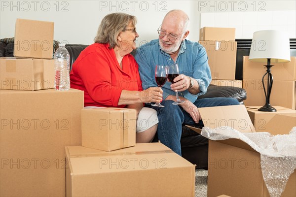 Senior adult couple toasting wine glasses surrounded by moving boxes