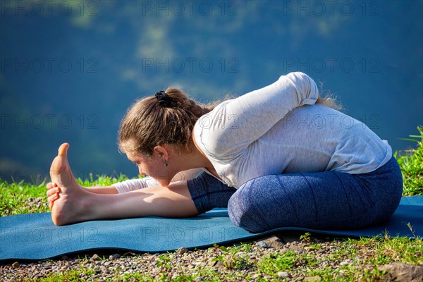 Woman doing Ashtanga Vinyasa yoga asana Ardha baddha padma paschimottanasana half bound lotus intense west stretch poser outdoors in mountains in the morning in Himalayas