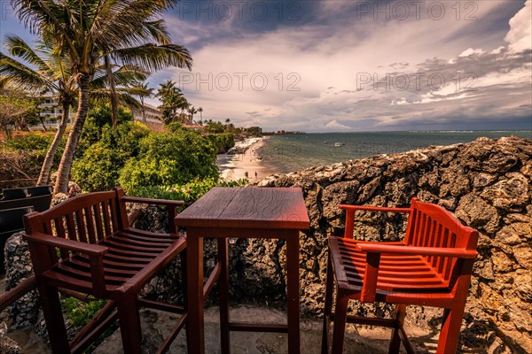 A view over two chairs with a table onto a beach and the sea. Sunset on the Indian Ocean