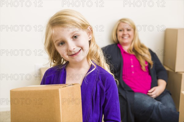 Happy young mother and daughter in empty room with moving boxes