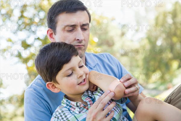 Loving father puts a bandage on the elbow of his young son in the park