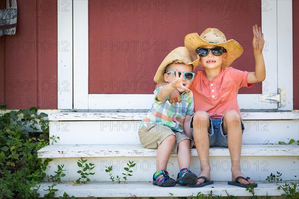 mixed-race chinese and caucasian young brothers having fun wearing sunglasses and cowboy hats