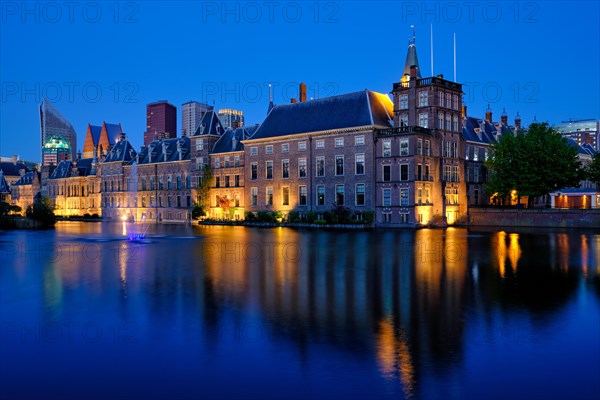 View of the Binnenhof House of Parliament and the Hofvijver lake with downtown skyscrapers in background illuminated in the evening