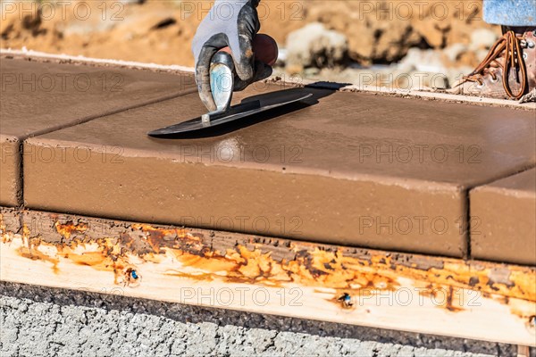 Construction worker using trowel on wet cement forming coping around new pool