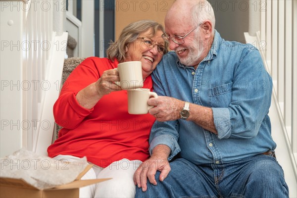 Tired senior adult couple resting on stairs with cups of coffee surrounded with moving boxes