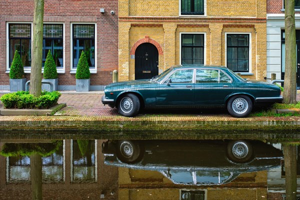 Old black retro car on canal embankment in street of Delft with reflection. Delft
