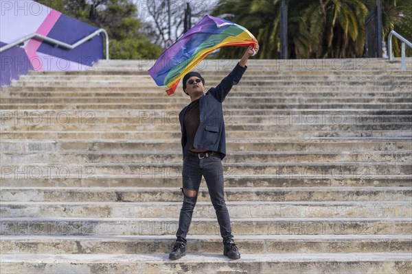 Lating gay male whit make-up on wearing fashionable hat holding lgbt flag. Concept of freedom and tolerance