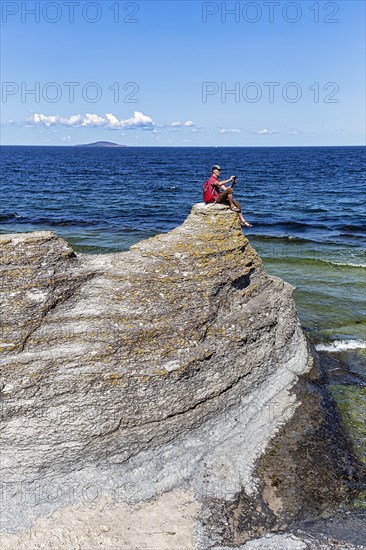 Hiker sitting on limestone pillar photographing landscape