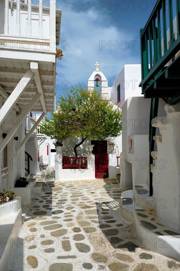 Picturesque scenic narrow Greek streets with traditional whitewashed houses with blue doors windows of Mykonos town and orthodox church in famous tourist attraction Mykonos island