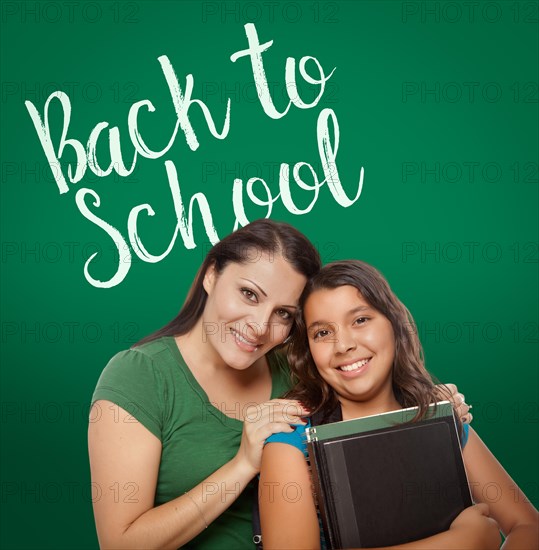 Back to school written on chalk board behind proud hispanic mother and daughter student