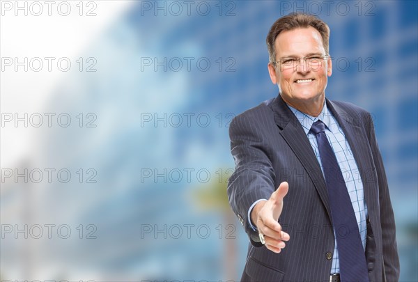 Smiling businessman reaching for hand shake in front of corporate building
