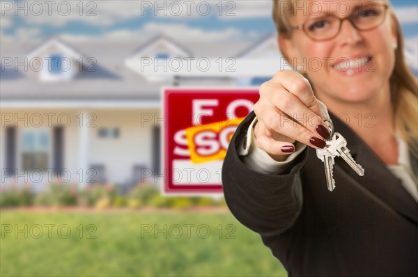 Real estate agent handing over new house keys with sold sign behind