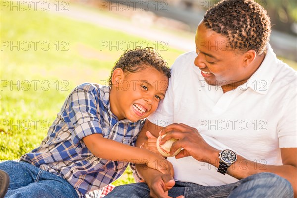 African american father and mixed-race son playing with baseball in the park