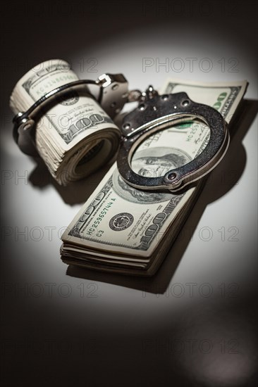 Handcuffs locked on roll of one hundred dollar bills under spotlight