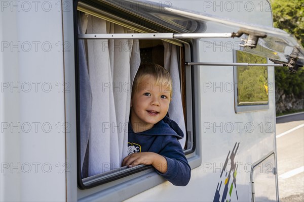 Happy small boy looking through the RV's window parked along the road