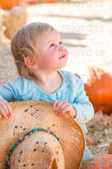 Adorable baby girl with cowboy hat in a country rustic setting at the pumpkin patch