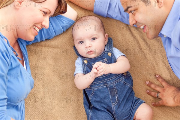 Young mixed-race couple laying with their infant on A blanket