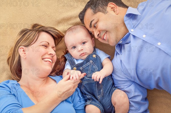 Young mixed-race couple laying with their infant on A blanket