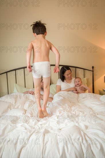 Young mixed-race chinese and caucasian boy jumping in bed with his family