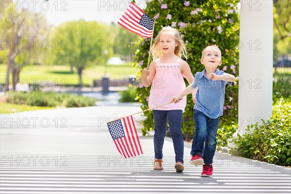 Young sister and brother waving american flags at the park