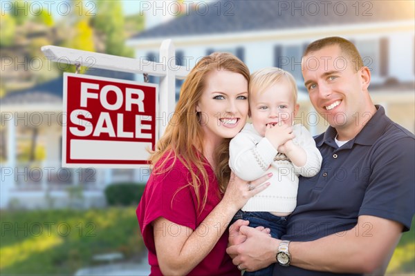Happy young military family in front of for sale real estate sign and new house