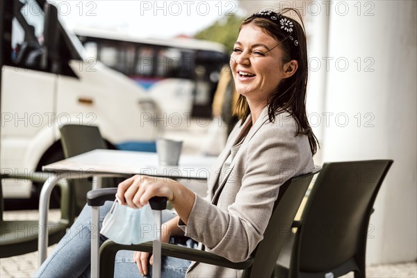 A young traveler with the luggage and protective mask sitting in the cafe and waiting for her bus to come