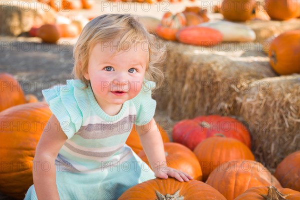 Adorable baby girl having fun in a rustic ranch setting at the pumpkin patch