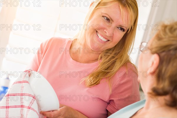 Senior adult woman and young daughter talking at sink in kitchen