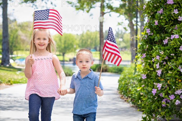 Young sister and brother waving american flags at the park