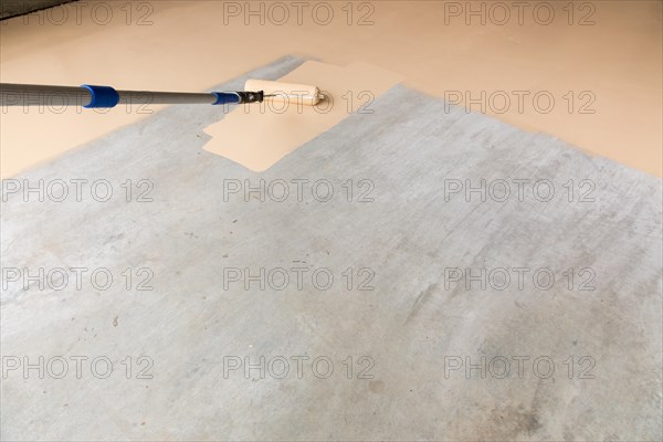 Worker painting floor of garage with roller
