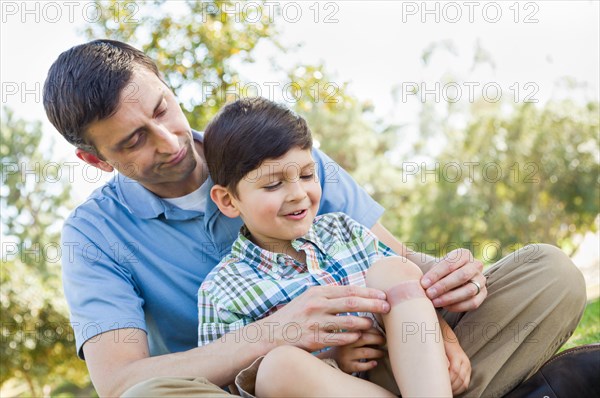 Loving father puts a bandage on the elbow of his young son in the park