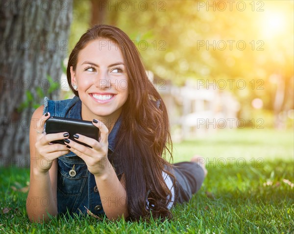 Attractive happy mixed-race young female laying in the grass texting on her cell phone outside