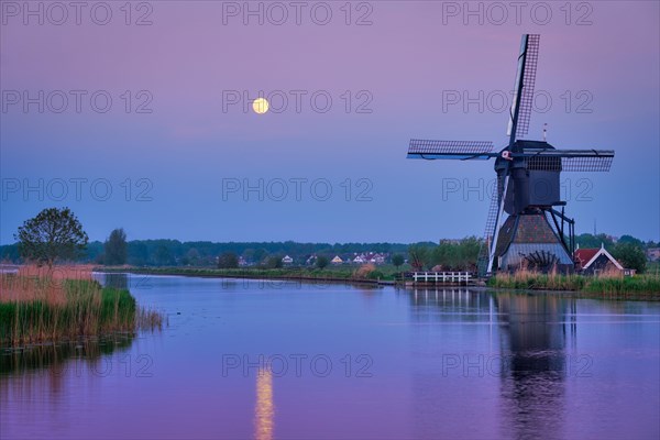 Netherlands rural landscape with windmills at famous tourist site Kinderdijk in Holland in twilight with full moon