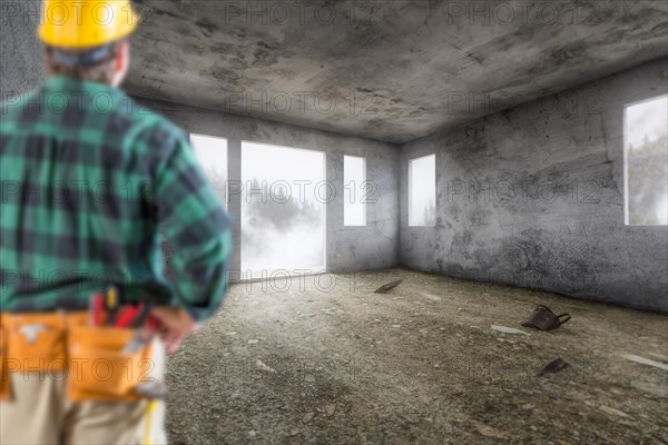 Contractor in hard hat and construction belt facing vacant empty abandoned room of house