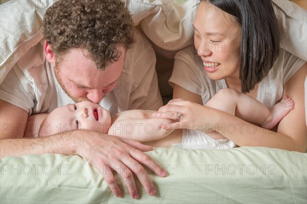 mixed-race chinese and caucasian baby boy laying in bed with his father and mother