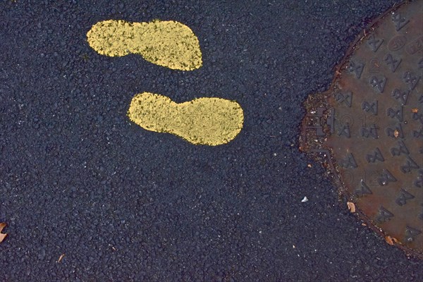 Two yellow footprints in the asphalt in front of manhole cover