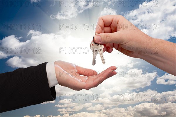 Male hand handing keys to female hand over dramatic clouds and sun rays