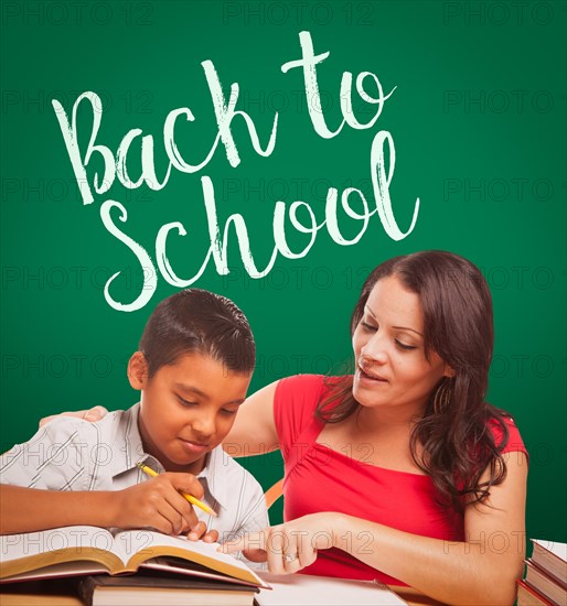 Back to school written on chalk board behind hispanic young boy and famale adult studying