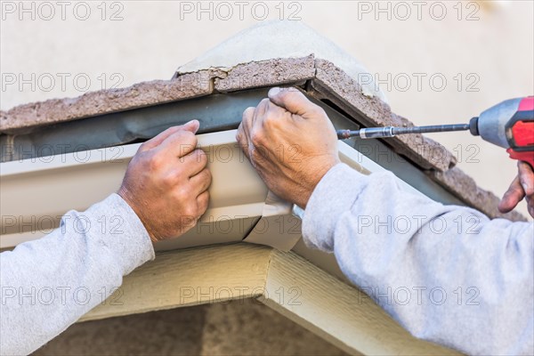 Workers attaching aluminum rain gutter to fascia of house