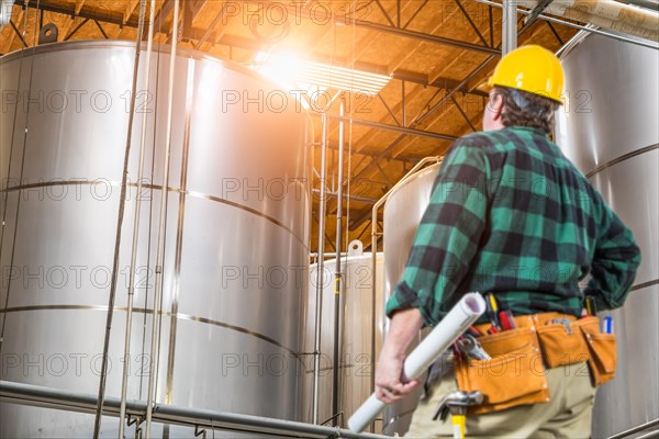 Man wearing hard hat looking up at large industrial tanks