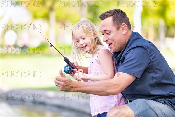 Young caucasian father and daughter having fun fishing at the lake