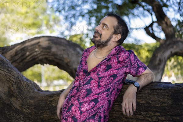 Bearded mature man wearing a fuchsia shirt with blurred green and blue background